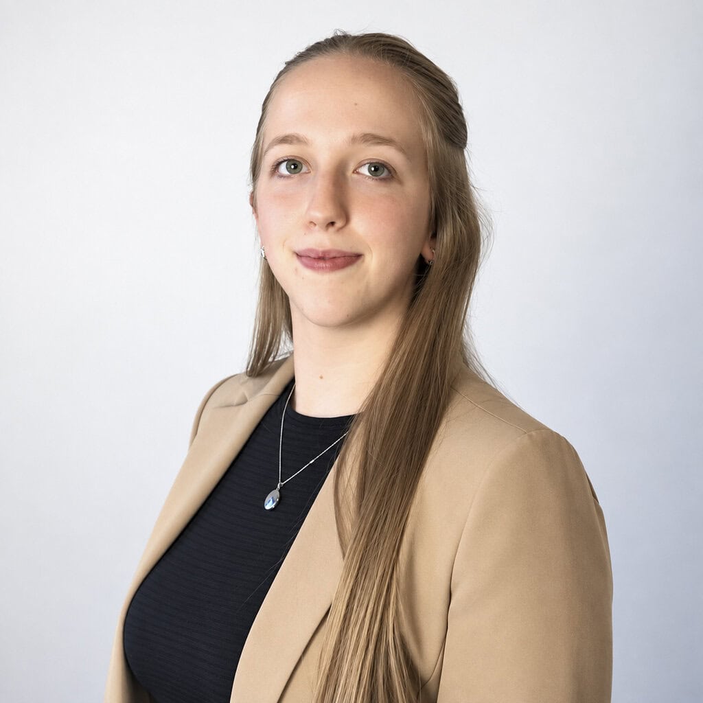 Young woman with long blonde hair wearing a beige blazer and black top.