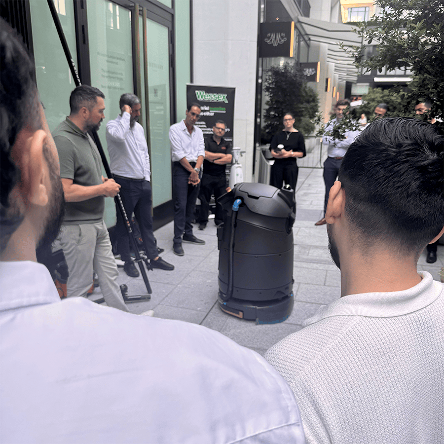 Group of people attending a demonstration of cleaning equipment outdoors.