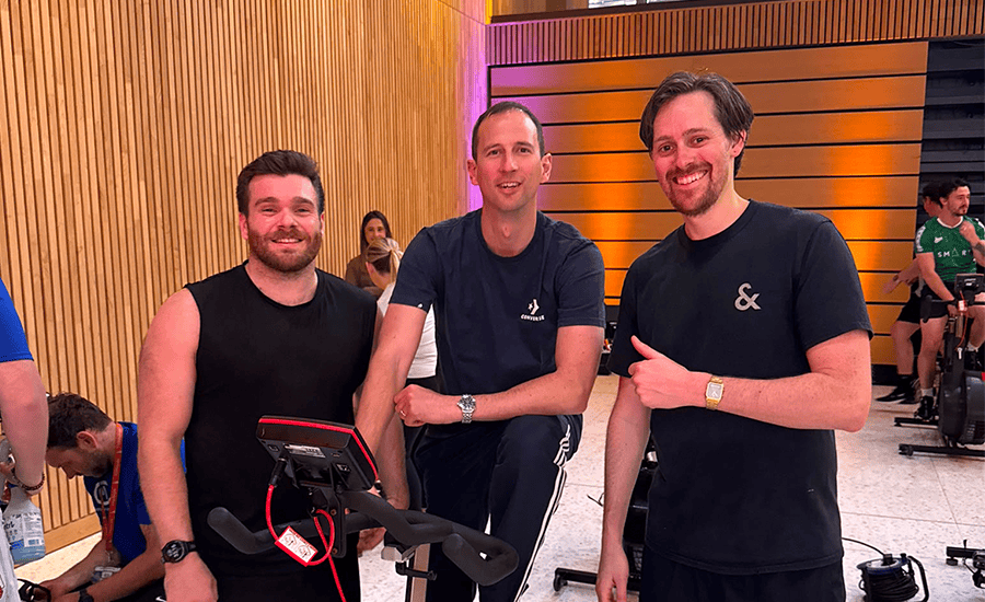 Three men smiling at a cycling event in a modern indoor space.